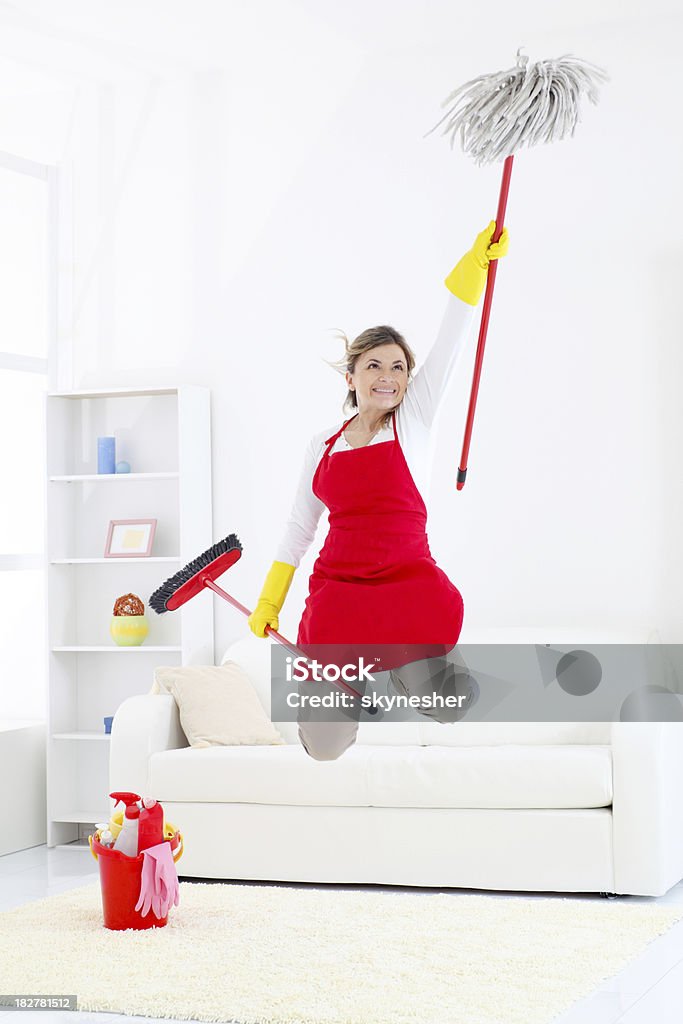 Happy cleaning lady jumping with broom and mop. Happy cleaning lady jumping with broom and mop in the bright room. One Woman Only Stock Photo