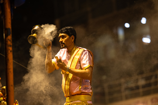 Varanasi, Uttar Pradesh, India - March 2023: Ganga aarti, portrait of hindu male priest performing holy river ganges evening aarti at dashashwamedh ghat in traditional dress with rituals.