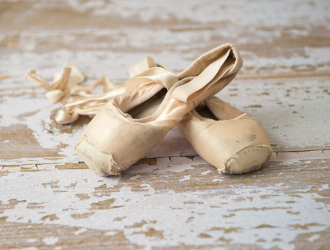 Old worn out ballet shoes on a wooden floor.