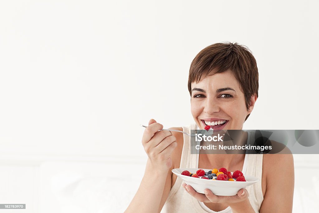 Jovem mulher sorridente comendo uma tigela de frutas - Foto de stock de Iogurte royalty-free