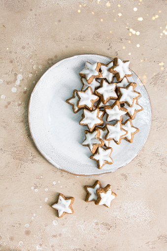 Top view of Christmas star shape ginger cookies with sugar icing on white plate with golden bokeh.