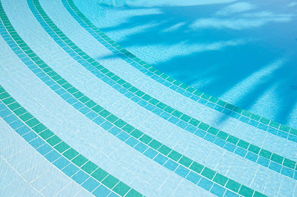Bright blue swimming pool background with curving steps leading to palm shadows