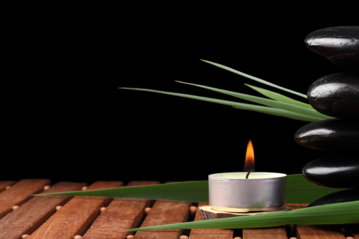 Massage Stones with reed leaves and candle - Isolated on Black - copy space