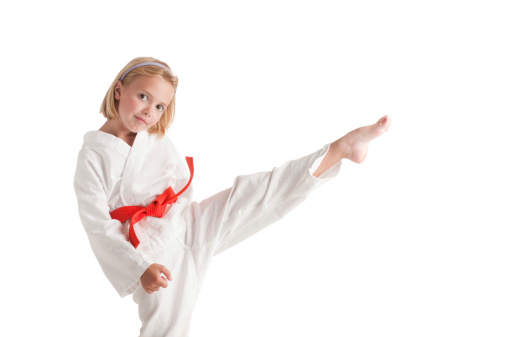 A young blond girl in a gi performs a front kick.