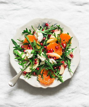 Rocket salad with tangerines, pomegranate, apples and mozzarella cheese on a light background, top view