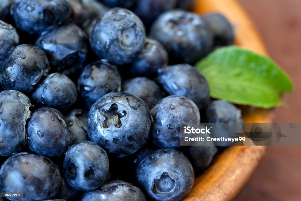 Fresh blueberries with green leaf accent in bowl Fresh blueberries in wooden bowl. Shallow DOF. Blueberry Stock Photo
