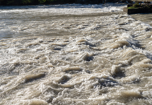 The river swollen after heavy rainfall and floodwater crashing through valley. The water flows fast from the high valley to the plain. General contest of a river in flood