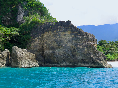 Rocky cliff off the coast of a tropical island in the blue sea.