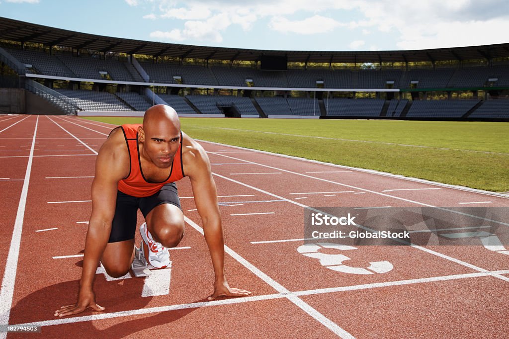 Atleta in posizione start sulla pista da corsa - Foto stock royalty-free di Blocco di partenza per l'atletica