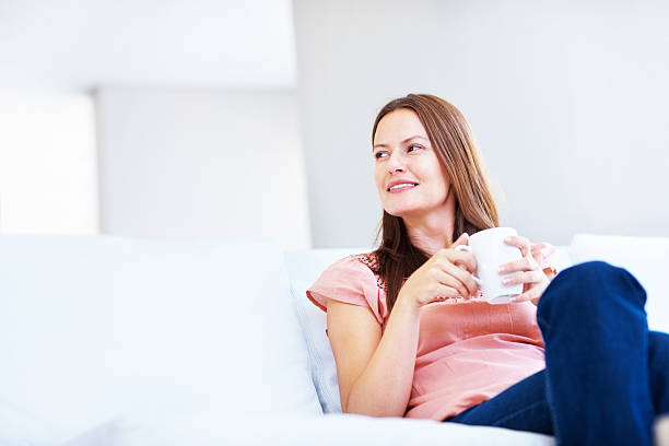 istock Contemplative lady holding a coffee cup while sitting on couch 182794970
