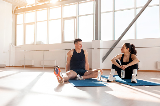 young athletic couple in sportswear in training are sitting on yoga mat and talking, man and woman are doing fitness in the morning and chatting on break