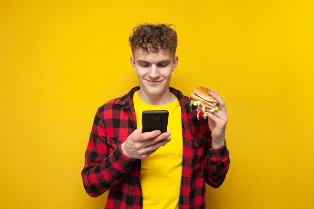 istock curly guy holds a big burger and uses a smartphone, a student eats fast food and looks into the phone 1827953366
