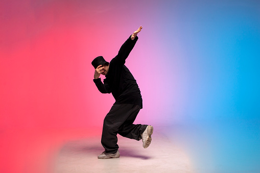 dancer dances hip hop in neon lighting, young guy moves his arms to the side and dances breakdance on red blue background, street rap style