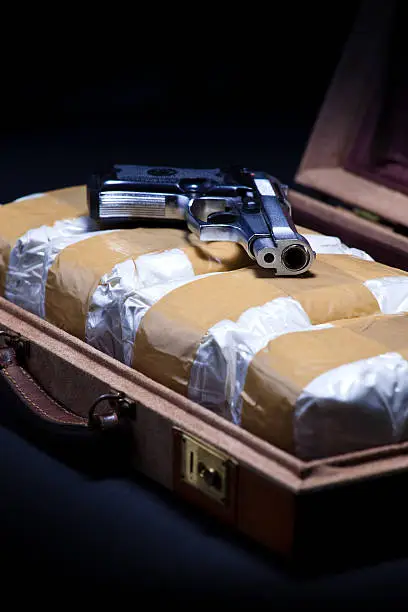 Still life of a briefcase full of bags of cocaine with a pistol laying on top of the contraband.  Angled shot.