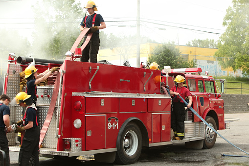Firefighters in action with fire hose on Fire truck. You can see smoke of fire in the background.