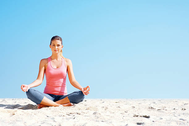 istock Young female sitting in lotus position on beach 182798635