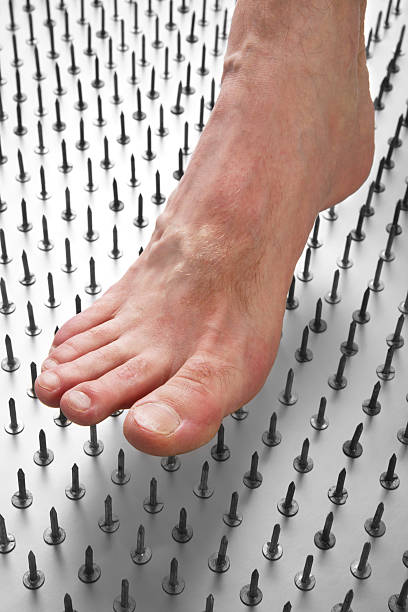 The concept of diabetic foot pain (or any foot pain) depicted by a foot stepping down on a field of nails.
