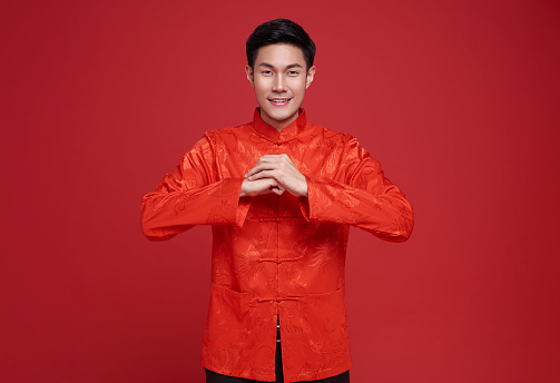 Happy Chinese new year. Asian man wearing red clothing with gesture of congratulation isolated on red background.
