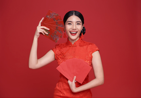 Happy Chinese new year. Asian woman wearing red dress holding angpao or red packet monetary gift isolated on red background.