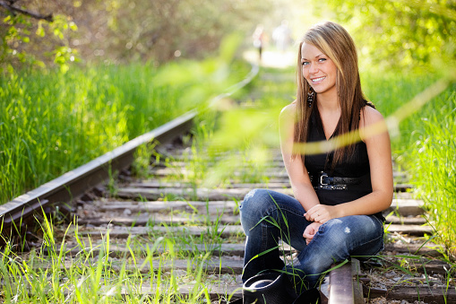 A pretty young woman sitting on abandoned railroad tracks.