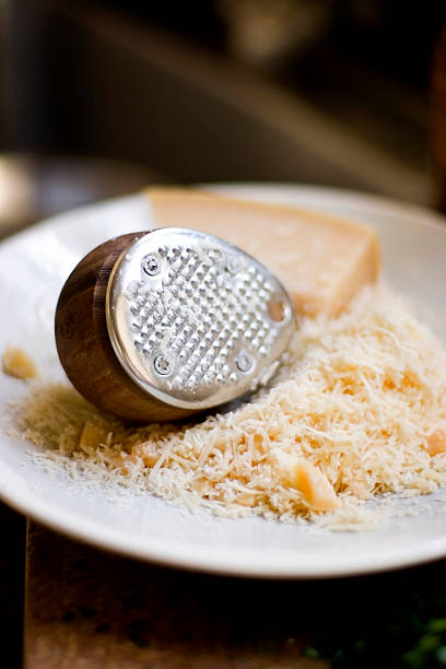 Modern cheese grater A rounded wooden cheese grater on a plate with grated parmesan cheese. pecorino romano stock pictures, royalty-free photos & images