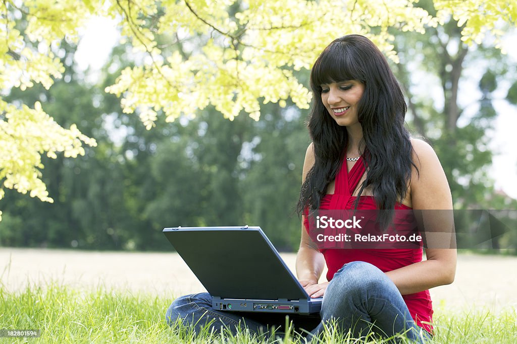 Kobieta siedząca z laptopa na trawie pod Baldachim drzew - Zbiór zdjęć royalty-free (Alternatywny styl życia)