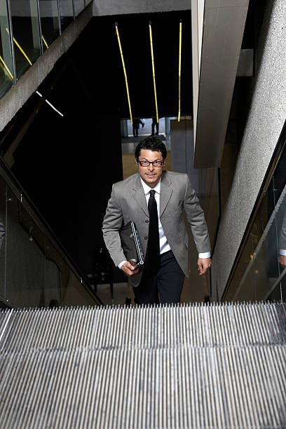 istock Young businessman running up escalator 182801971