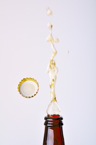 Beer splashing from the bottle with the cap flying in the air against a white background