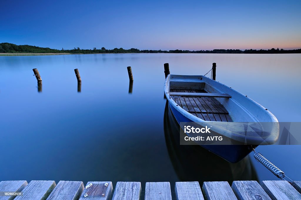 Calm Lake with Fishing Boat Tied to Dock after sunset Beach Stock Photo