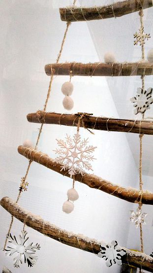 White snowflake shape figurines hanging from rustic Christmas tree, white wall background. Christmas decoration. Galicia, Spain.