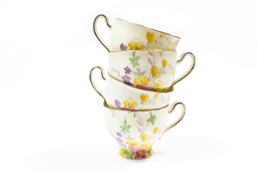 Four antique floral pattern teacups one on top of the other on white background