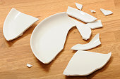A broken white ceramic plate on a wooden floor