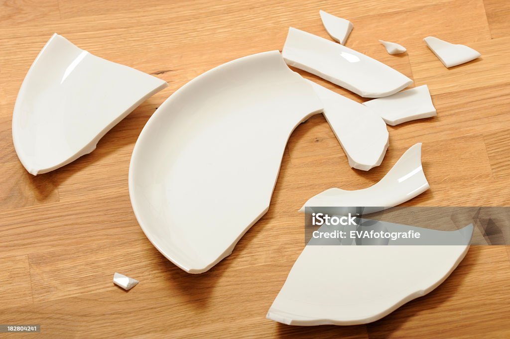 A broken white ceramic plate on a wooden floor White plate lies broken on the floor. Broken Stock Photo
