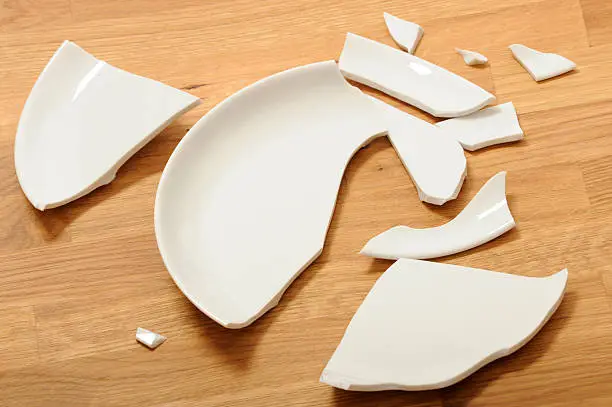 Photo of A broken white ceramic plate on a wooden floor