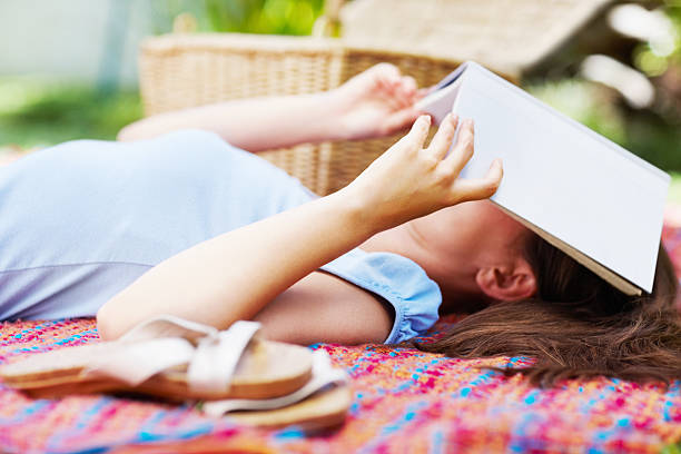istock Woman covering her face with book while lying on carpet 182805381