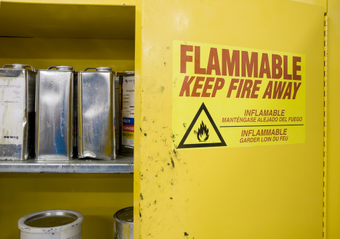 Open cabinet containing hazardous chemicals. Cans are dented and leaking with warning label visible.