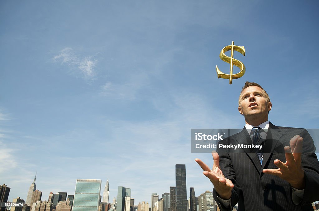 Businessman Catches Golden Dollar at City Skyline Businessman holds out his hands to catch a golden dollar falling in front of a city skyline Adult Stock Photo