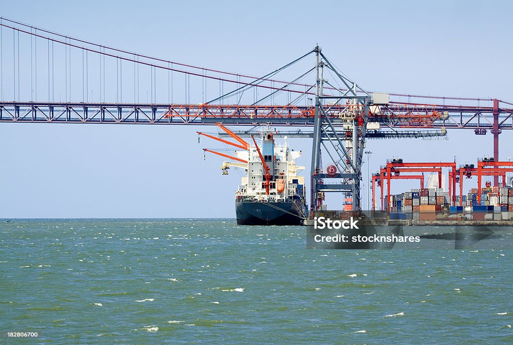 Container Freight "Container ship moored at the dock, being loaded with containers at Lisbon, Portugal, with April 25 Bridge across the River Tagus in the background. Good copy space.." Commercial Dock Stock Photo