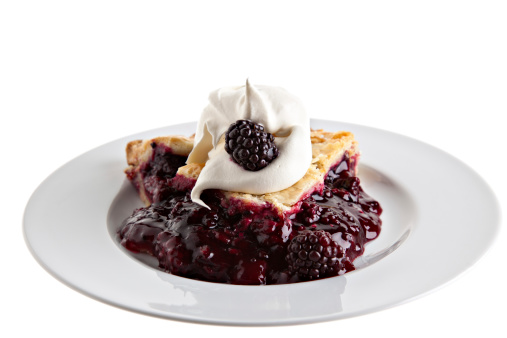 Boysenberry pie with whipped cream on a white background.