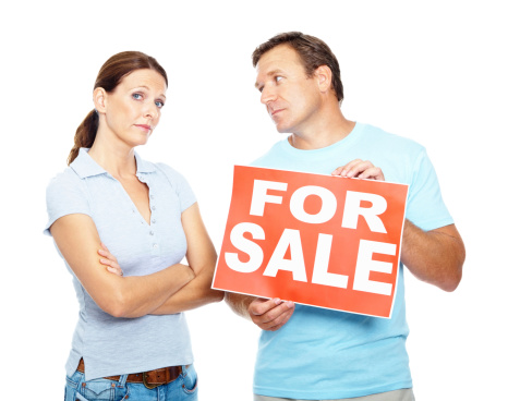 Upset mature man holding a sale sign board and looking at his wife against white background