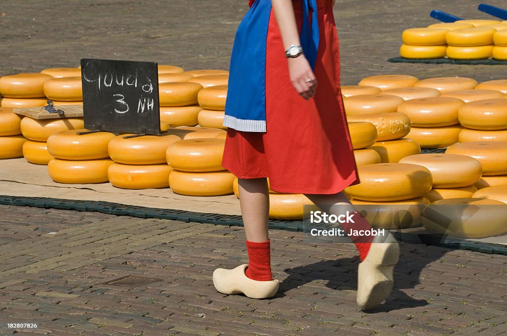 Alkmaar Cheese Market "A girl in traditional Dutch clothes walking on wooden shoes  in front of piles of Gouda cheeses on the cheese market in Alkmaar, Netherlands" Netherlands Stock Photo