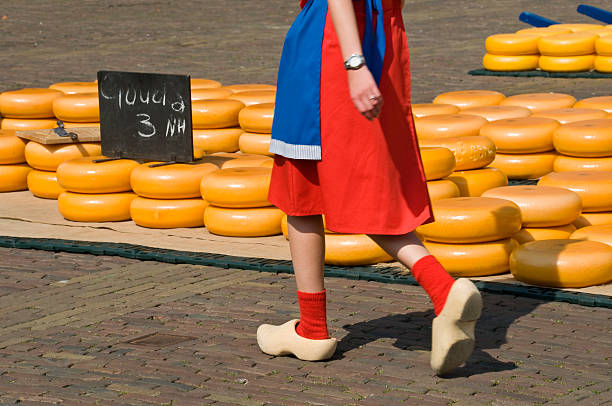 Alkmaar Cheese Market "A girl in traditional Dutch clothes walking on wooden shoes  in front of piles of Gouda cheeses on the cheese market in Alkmaar, Netherlands" cheese market stock pictures, royalty-free photos & images