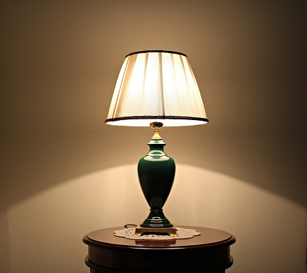 Coassic elegant lamp with illuminated lampshade on a small round table in the room.