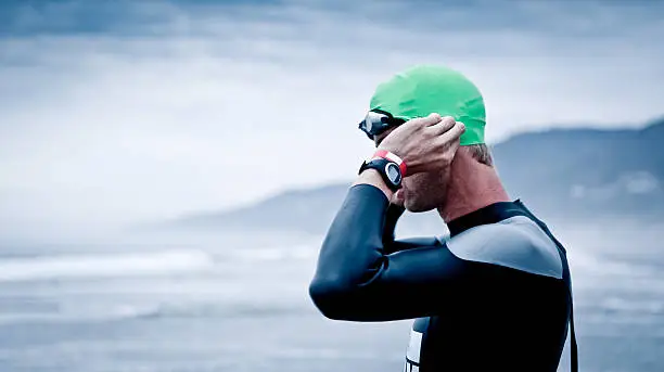 Triathlete stands on a shoreline before a long distance open water swim.