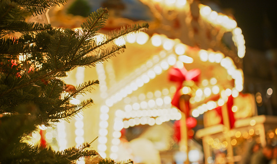 In the heart of Graz,Styria,Austria,a cropped view captures the festive allure of a Christmas tree against the backdrop of a defocused carousel at the night market. The twinkling lights create a mesmerizing atmosphere with the joyful dynamism of the carousel