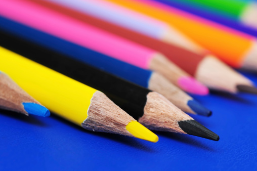 Horizontal row of colorful pencils on grey paper background. School supplies in colores of rainbow on blackboard. Kid's stationery with black copy space. Back to school backdrop.