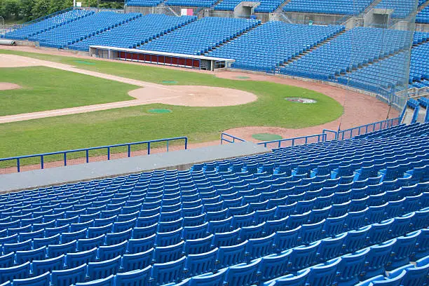 Looking across many rows of empty seats towards the homeplate in a baseball park.