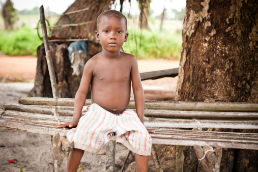 An African boy sitting on a bamboo bench.