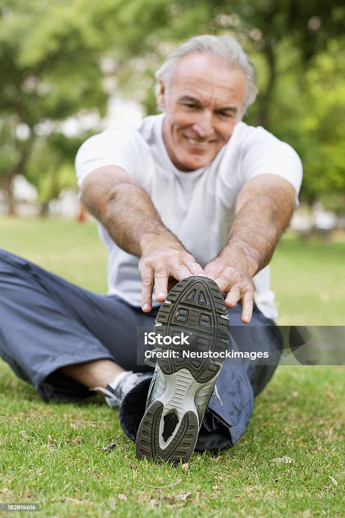 Senior Male Stretching in the Park Senior man stretches in the park by touching his toes. He is dressed in active wear. Vertical shot. Active Seniors Stock Photo