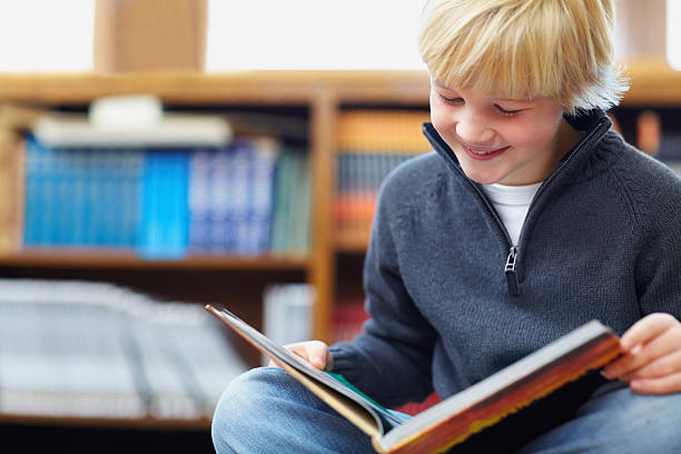 glücklich hübsch schule junge liest ein buch in der bibliothek - elementary student school children child schoolboy stock-fotos und bilder